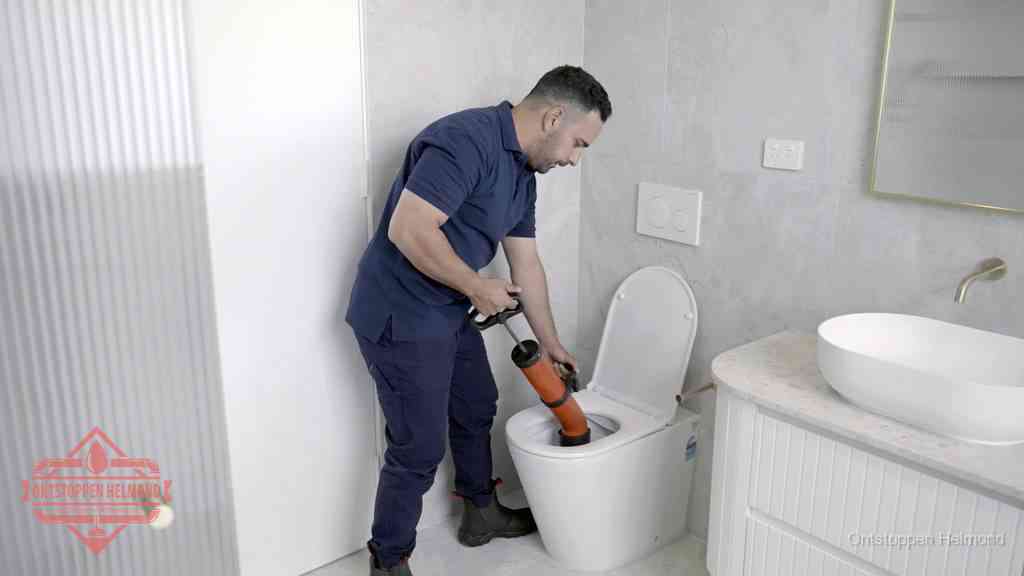 Een monteur buigt over een wandcloset en duwt met de hand een persluchtontstopper in de toiletpot om de verstopping handmatig los te maken in Helmond