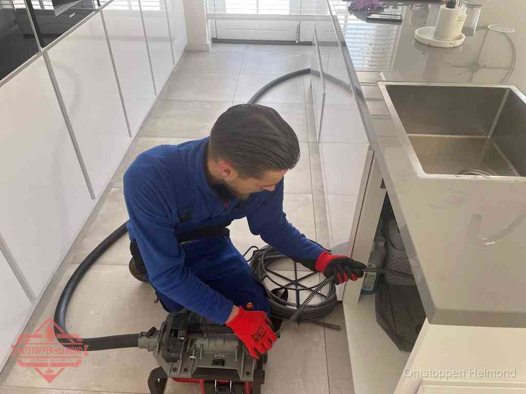 Een monteur ontstopt de keukenafvoer onder de spoelbak met een elektrische veermachine in Helmond