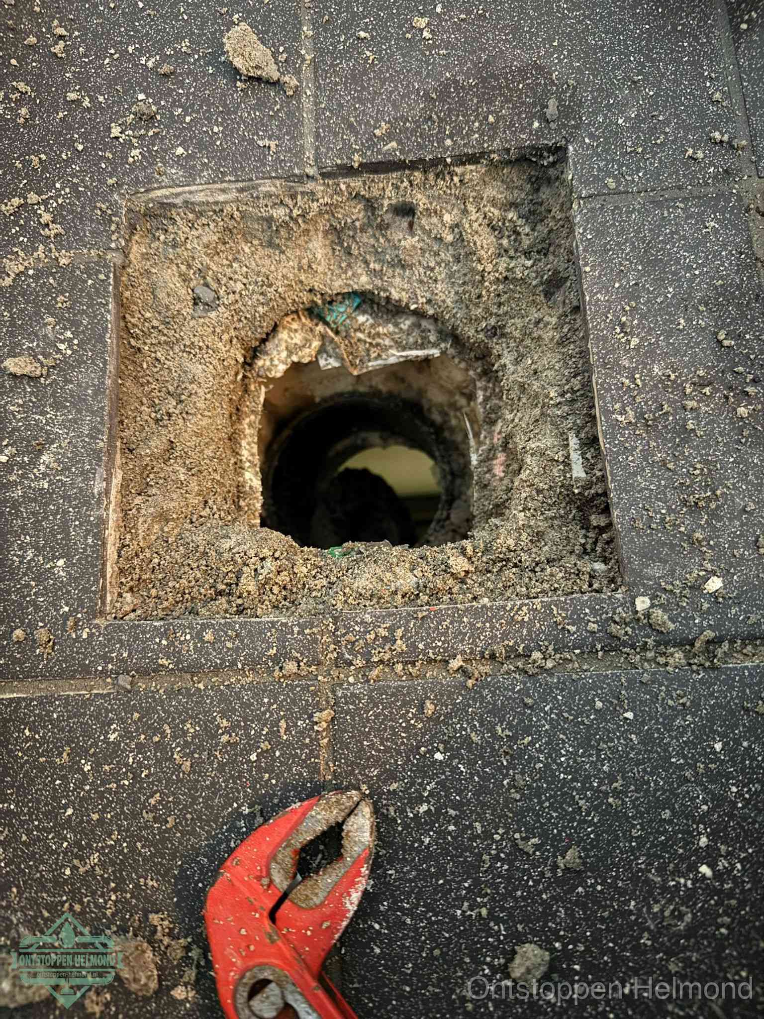 Een geopend rioolputje in een betontegelvloer met losgemaakt rooster en een zichtbare ronde afvoerbuis, het achterhalen waar de afvoerverstopping zit in Helmond