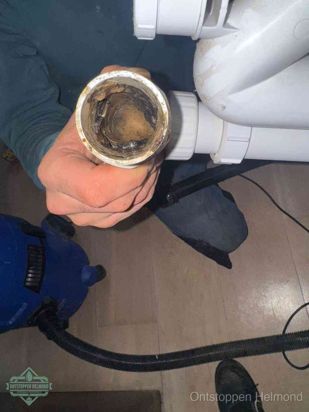 Een hand houdt een losgekoppeld PVC-afvoerbuisstuk vast dat van binnen volledig is dichtgeslibd met vet, vuil en aanslag, de meest voorkomende oorzaak van een verstopte afvoer in Helmond