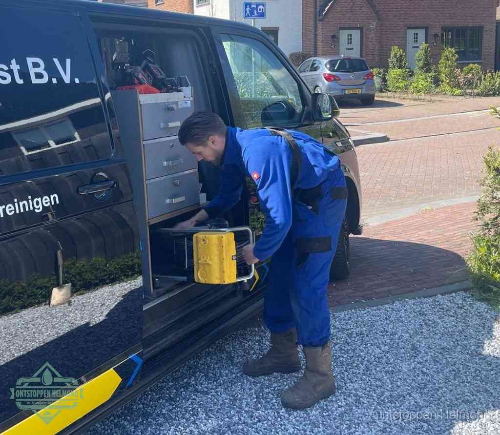 Een monteur pakt buiten op de oprit gereedschap uit de bedrijfsbus, het moment om een professional in te schakelen voor een verstopte afvoer in Helmond