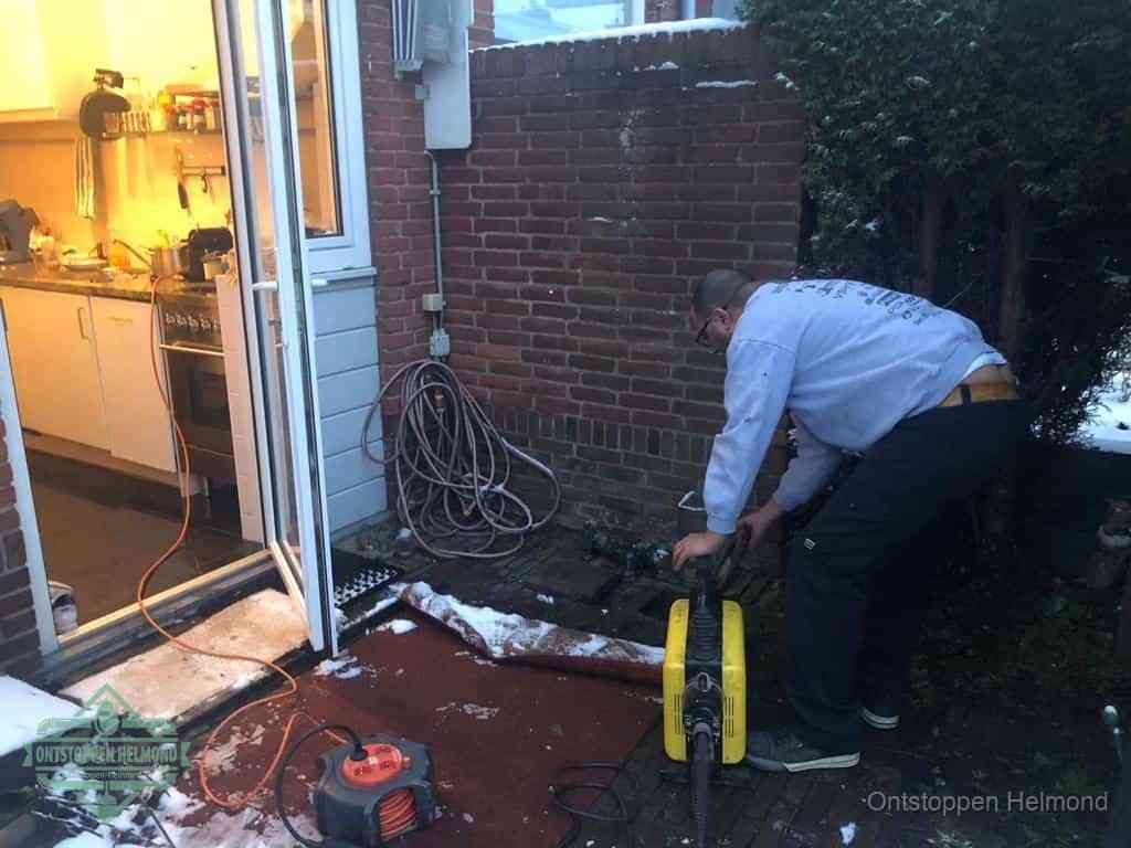 Een monteur werkt buiten bij een open riool-/grondput met een elektrische ontstoppingsmachine om een verborgen afvoerprobleem op te sporen in Helmond