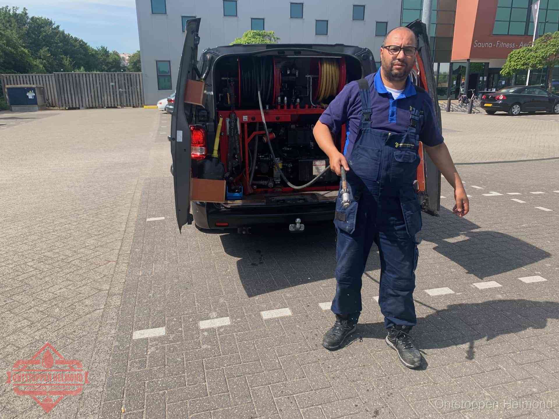 Een monteur bij zijn bestelbus met een hogedruk- en rioolreinigingsunit, klaar om de oorzaak van terugkerende wc-verstoppingen aan te pakken in Helmond