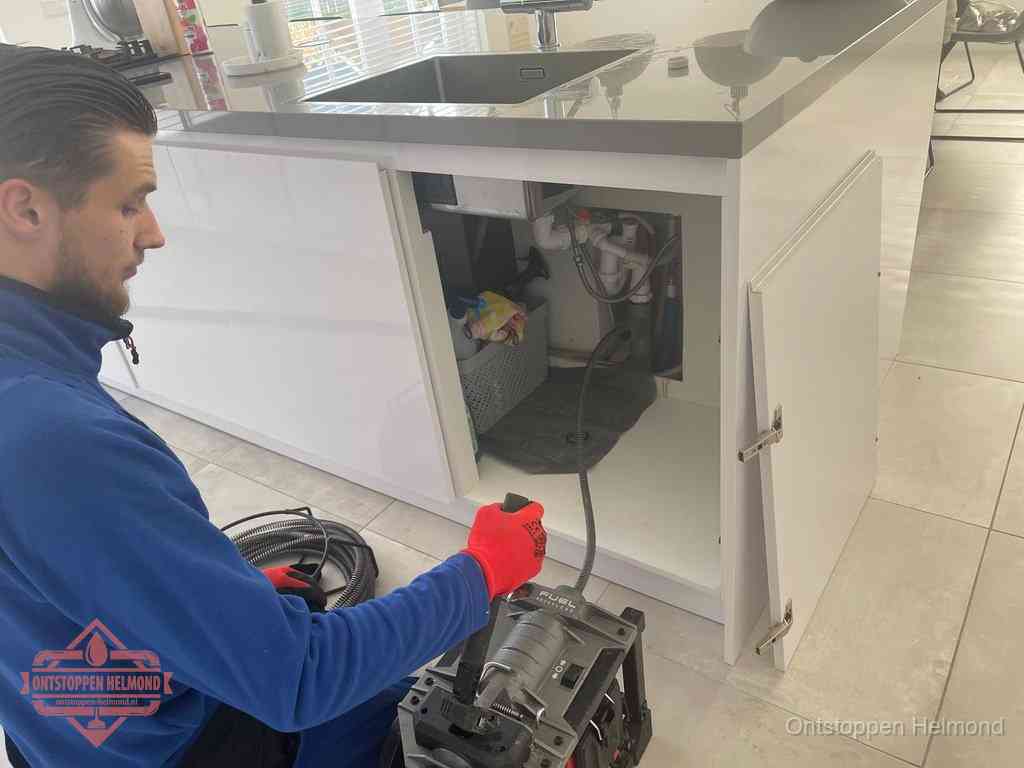 Monteur ontstopt met een veermachine een verstopte afvoer onder de gootsteen in Helmond