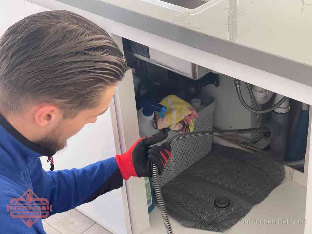 Een monteur voert een flexibele ontstoppingsveer in de afvoer om een verstopping voorbij de bocht van het toilet te bereiken in Helmond