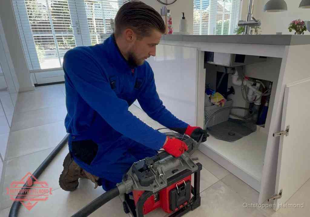 Een monteur voert een professionele elektrische ontstoppingsmachine in de afvoer onder de spoelbak tijdens het gootsteen ontstoppen in Helmond