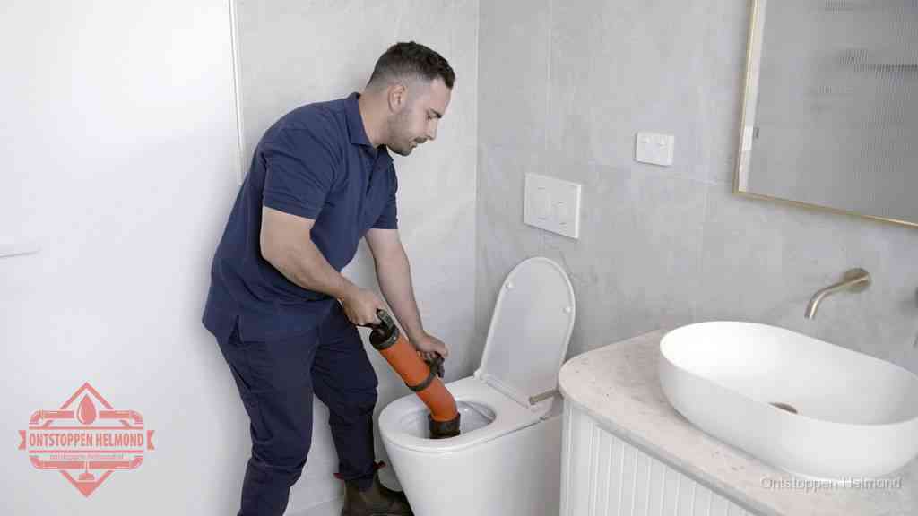 Een man gebruikt een handmatige luchtdruk-ontstopper in een modern betegeld toilet om zelf de wc te ontstoppen in Helmond